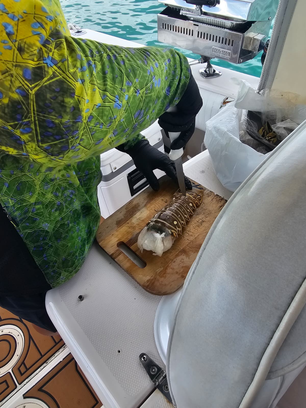 Captain prepping fresh Caribbean lobster tails on a wooden cutting board onboard the charter