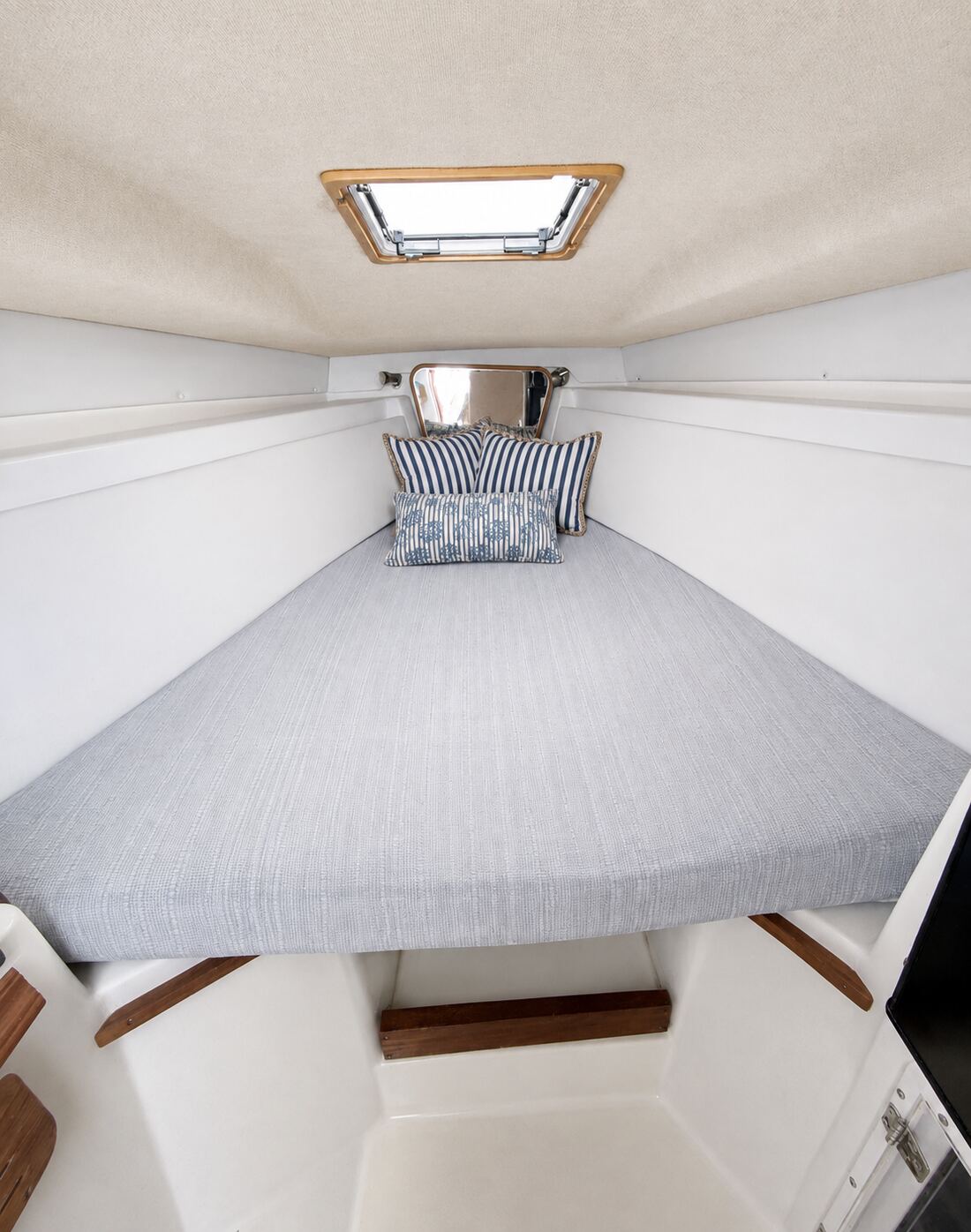 V-berth cabin below deck on the Contender 38 with a cushioned berth, striped pillows and an open overhead hatch