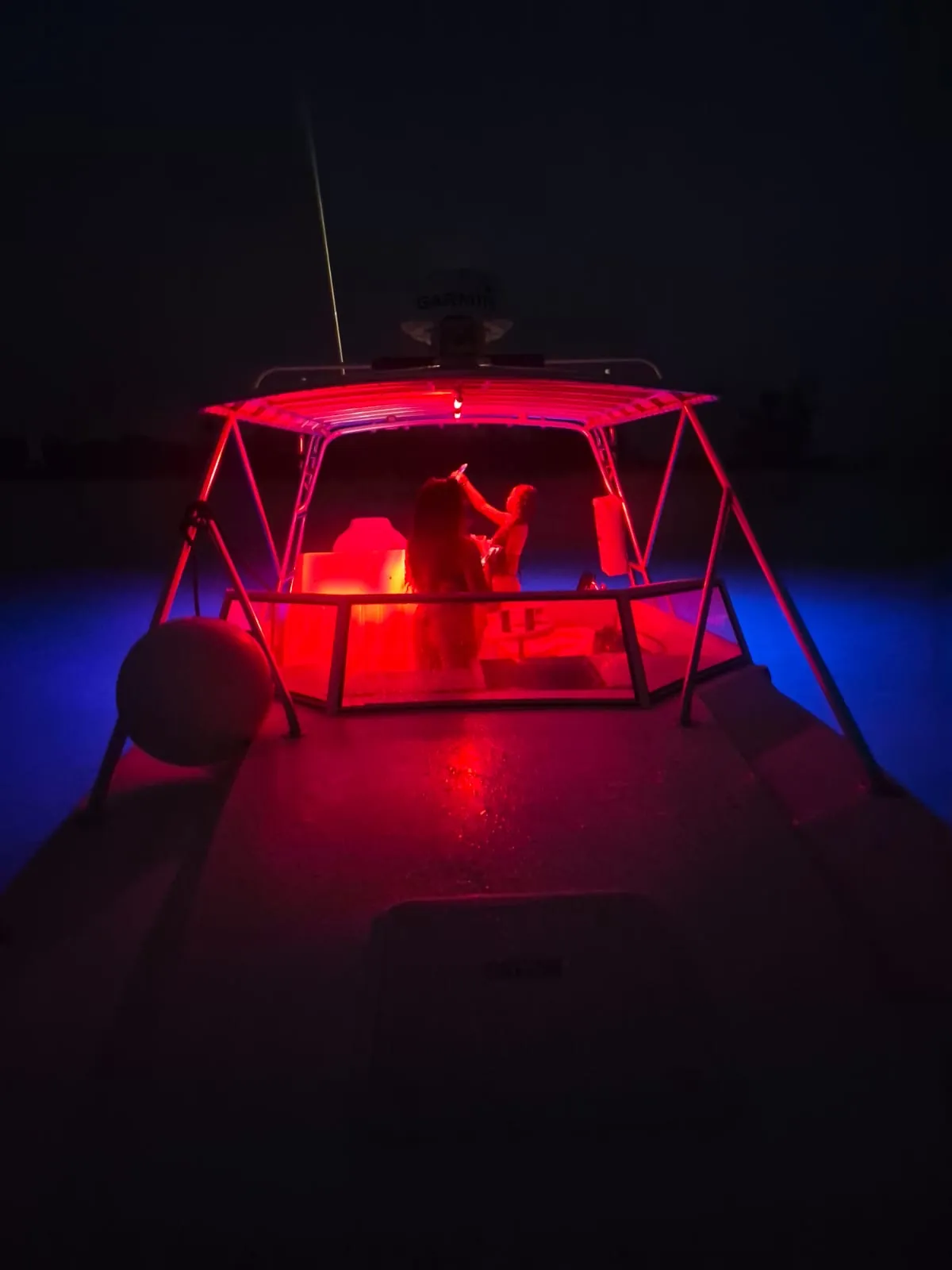 Contender 38 center console at night with the hardtop lit red and blue underwater lights glowing on both sides of the hull