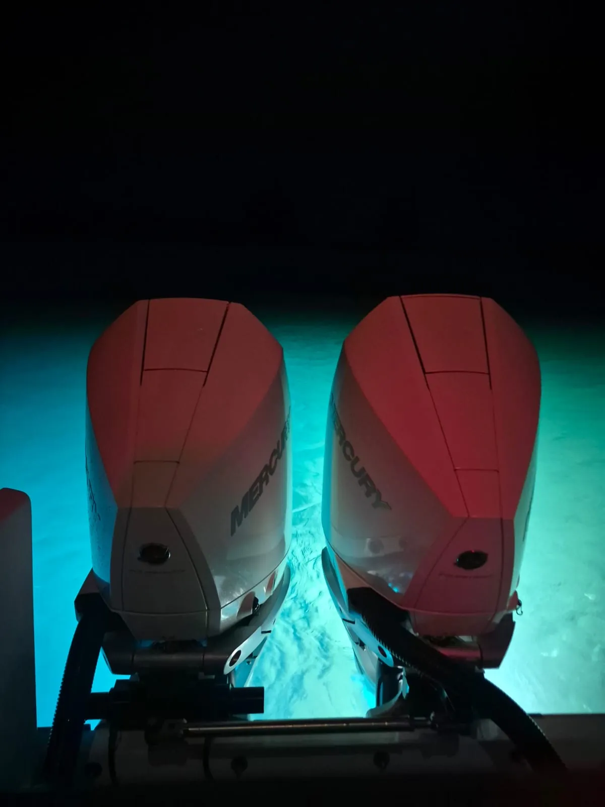 Close view of the twin Mercury outboards over turquoise water lit from below by the boat's underwater lights