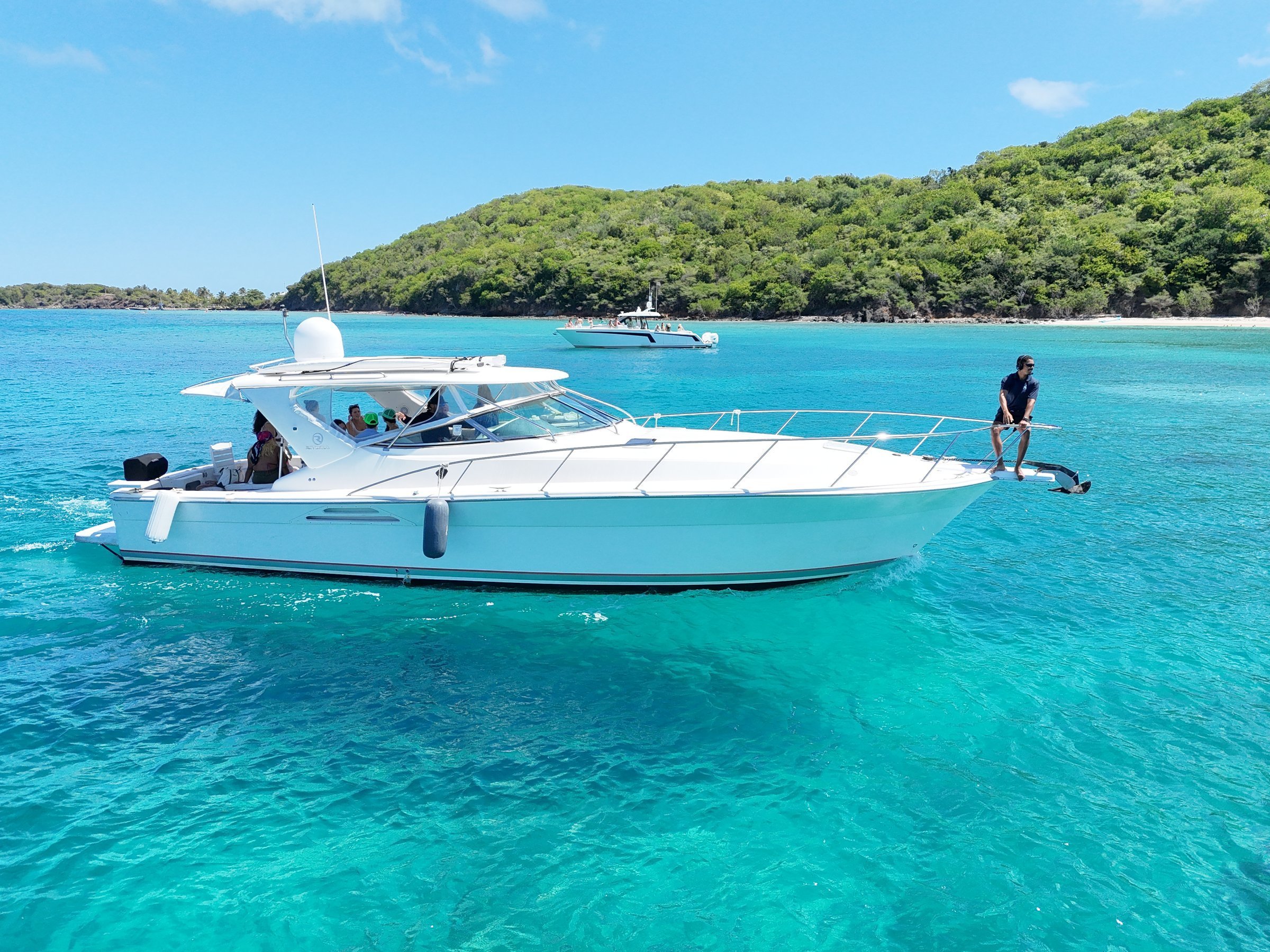 Sport yacht anchored at Caribbean sandbar with guest sitting on the swim platform, turquoise water
